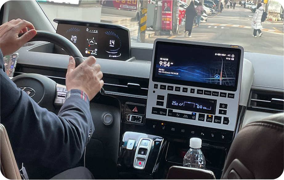 An EV taxi driver at the wheel, hand on the steering wheel, the vehicle infotainment screen lit beside them.